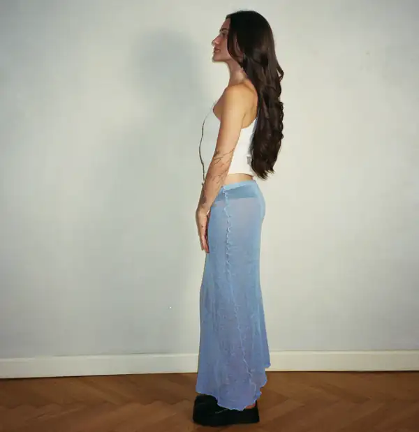 Right profile, full-length: white top and blue skirt, hair drawn over the shoulder.