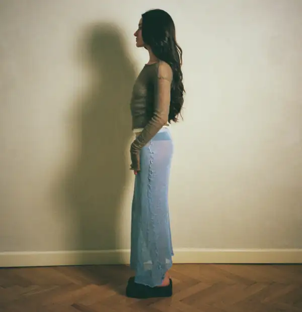Rear three-quarter: olive long-sleeve and blue skirt, the skirt's seam line running down the back.