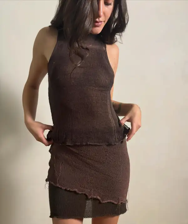 Detail crop, chest to thigh: brown sheer halter over a brown knit mini skirt, hands at the waist. The highest-resolution frame of this post.