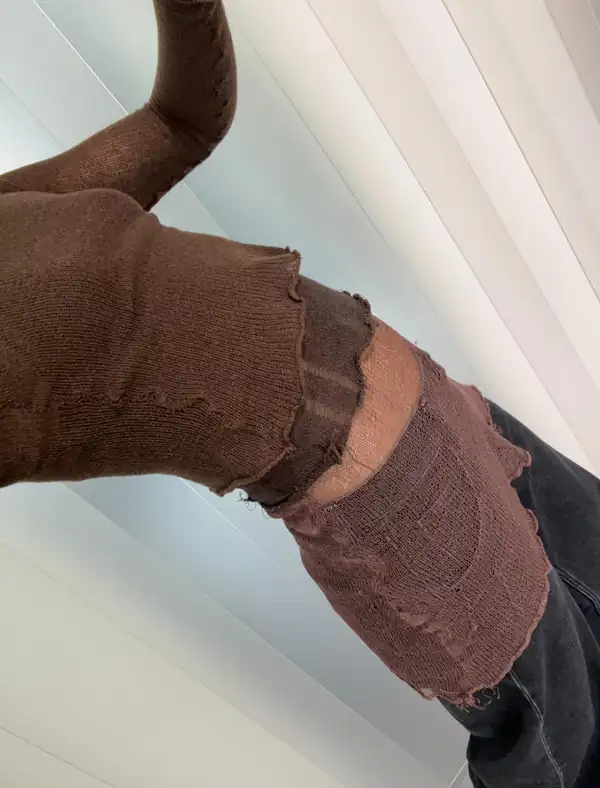 Extreme close, tilted: brown knit sleeve and brown knit skirt over dark jeans.