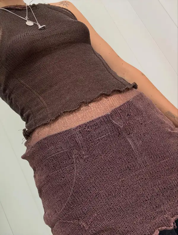 Close torso: brown knit top with a rolled hem over the brown knit skirt, bare midriff, silver pendants.