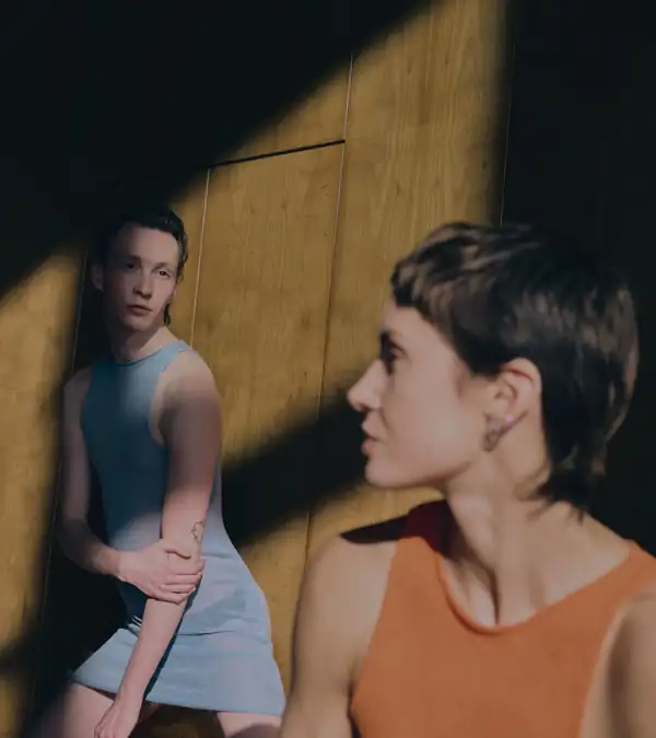 Two performers, one seated and one in profile, blue and orange knit against yellow and wood.
