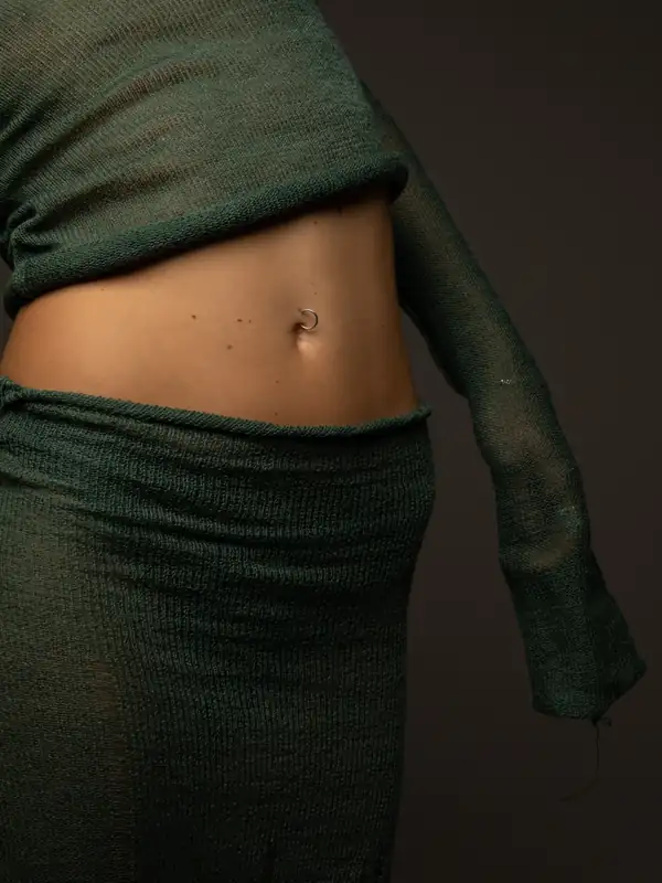 Close: dark green sheer knit at the waist, bare midriff, navel piercing.