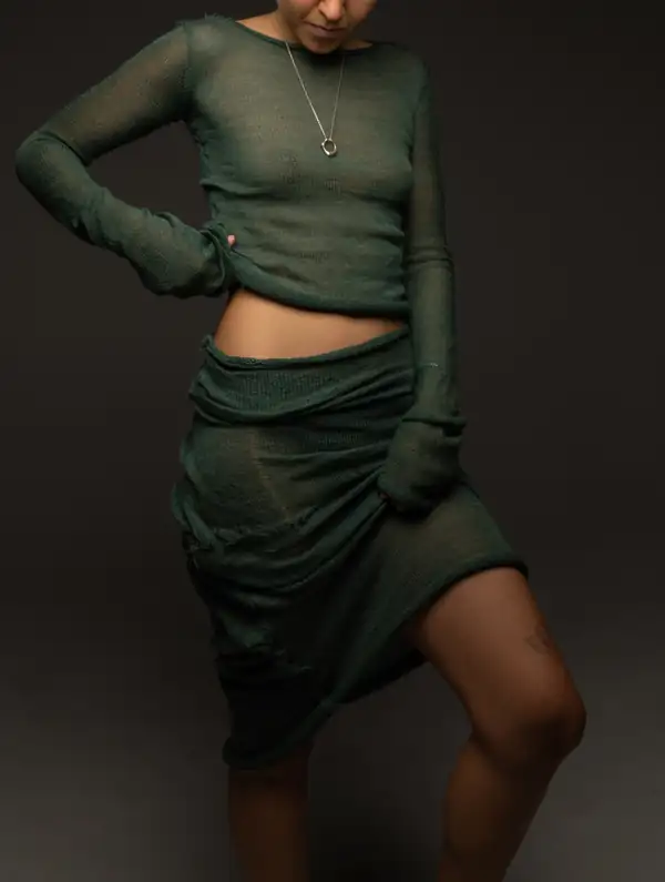 Three-quarter: dark green sheer long-sleeve and wrapped skirt, leg lifted, silver necklace.