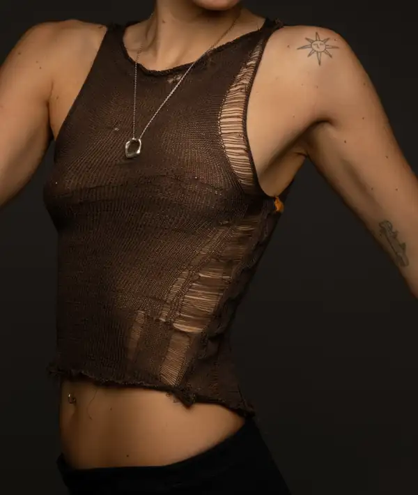 Torso, front: brown sheer knit vest with vertical ladder/ripped detail, silver pendant, black waistband. Source of the site's Top image.