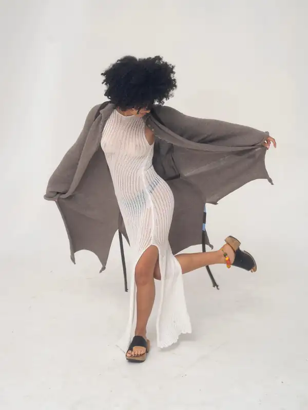 In motion: taupe knit long coat flaring open over a white ribbed knit long dress, black sandals.