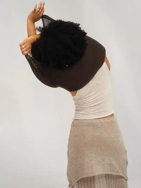 Bent forward with the brown top pulled up over the head, white knit tank and taupe skirt beneath.