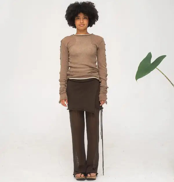 Full-length front: tan knit long-sleeve with buttoned slit sleeves, brown knit skirt over sheer brown trousers, green leaf prop.
