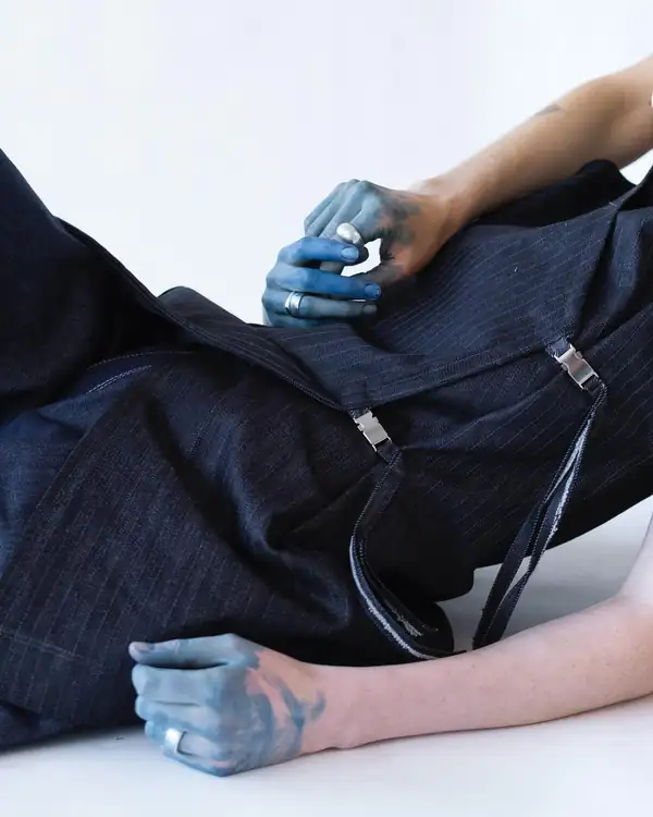 Close: hands with indigo-stained fingers on an indigo denim garment with metal clasps.