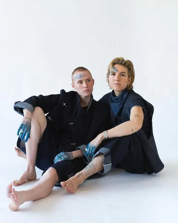 Two models seated on the floor in indigo denim pieces with indigo body paint.