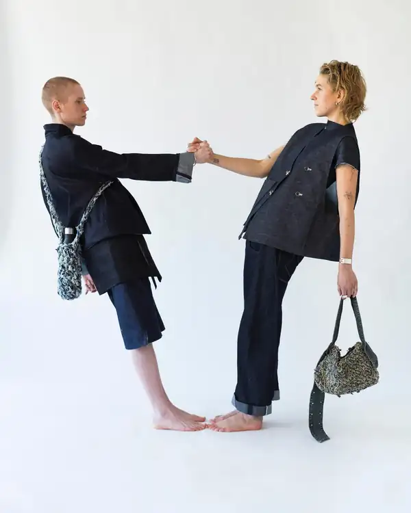 Two models, one leaning and holding hands: indigo denim jacket and shorts, knitted bag.