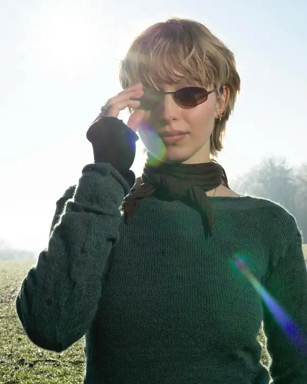 Portrait into the sun with heavy lens flare: green knit top and dark scarf, sunglasses.