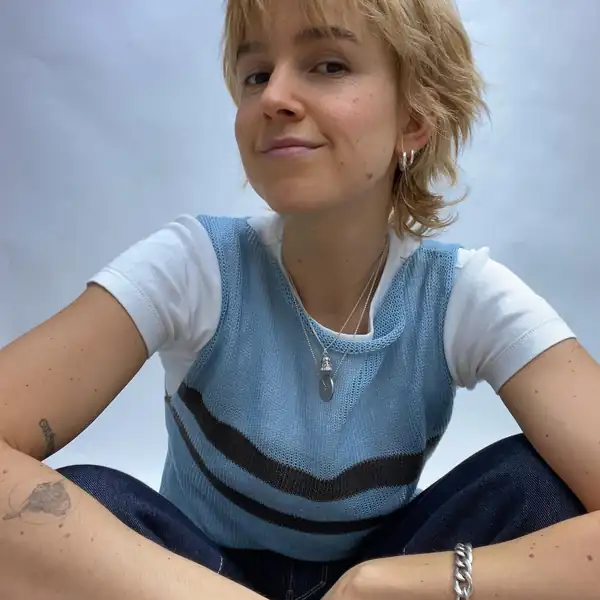 Seated close portrait: the blue knit tank with dark stripes over a white tee, crystal pendant.