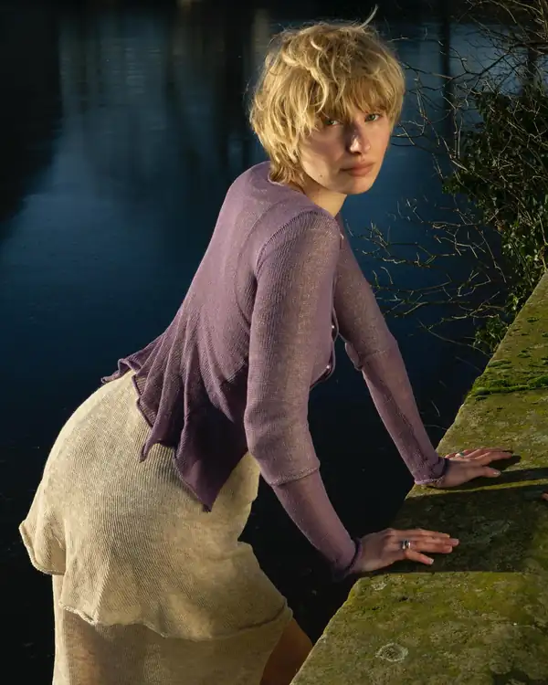 Leaning on a mossy wall: the purple cardigan and cream skirt.