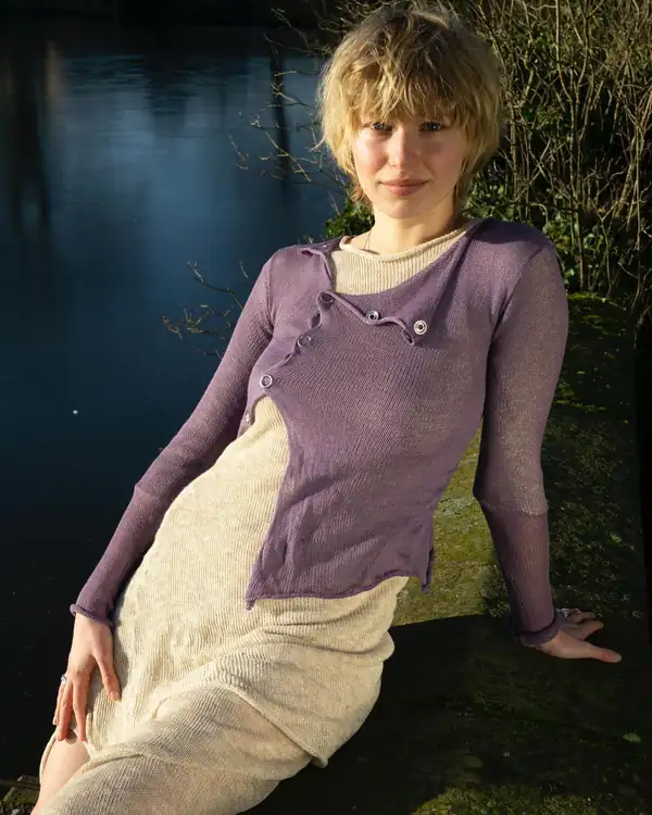 Seated portrait: the purple cardigan over the cream skirt, water behind.