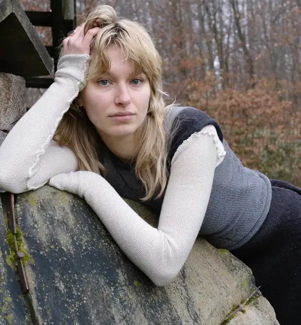 Leaning on a stone: portrait, cream long sleeves and a grey knit bodice.