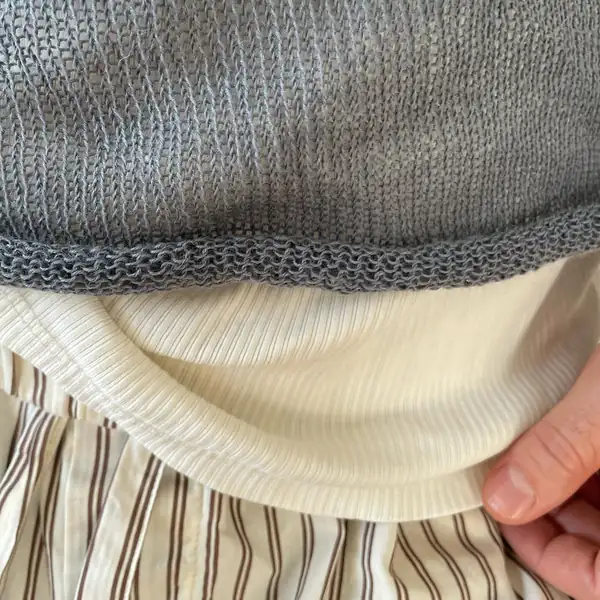 Very close: the grey knit's rolled hem edge over cream ribbing.