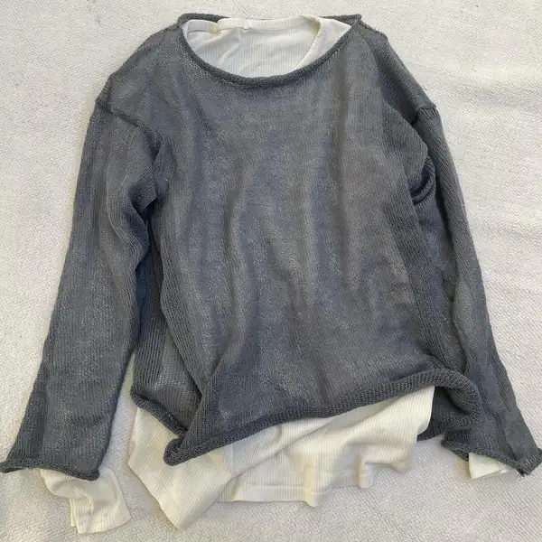 Flat lay on sand: the grey knit jumper laid over the cream long-sleeve.