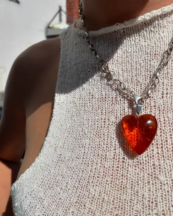 Extreme close: cream knit halter top with a silver chain and an amber glass heart pendant.