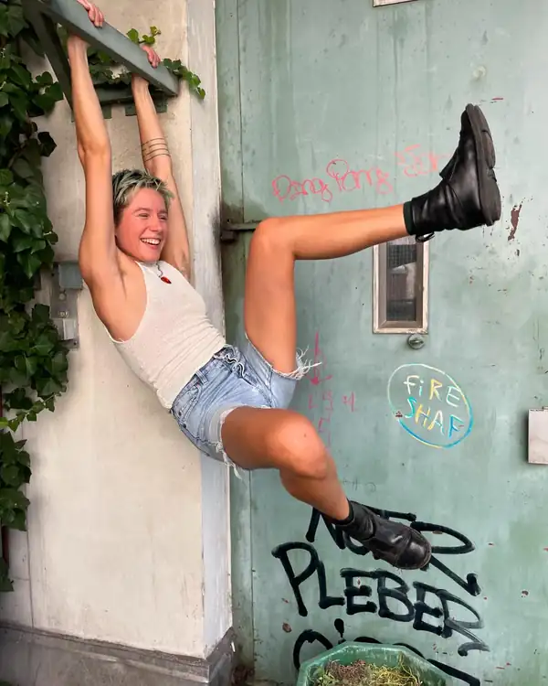 Mid-air, braced between a wall and a green door: the cream knit halter and denim shorts, laughing.