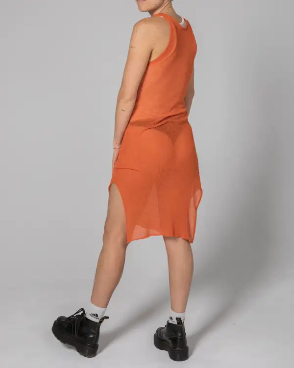 From behind: orange sheer knit tank dress with a rear slit, black trainers, grey studio.