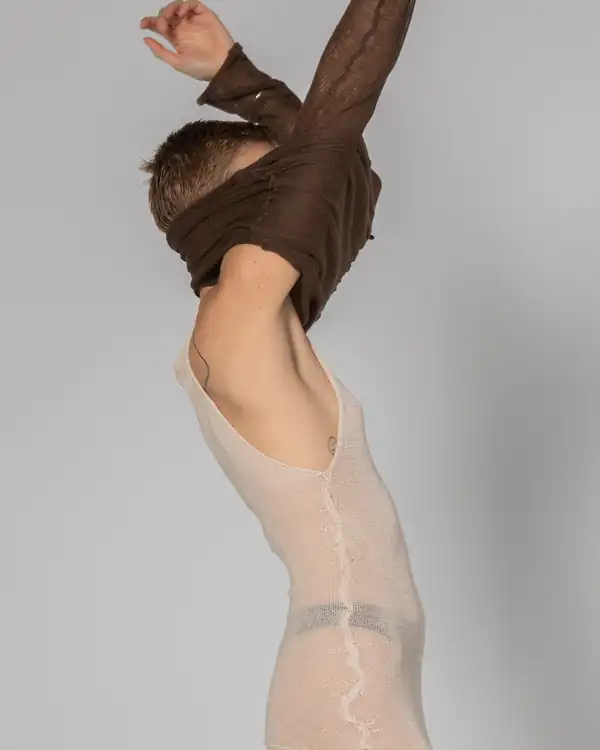 Pulling a brown knit top over the head, revealing a cream knit slip dress beneath.