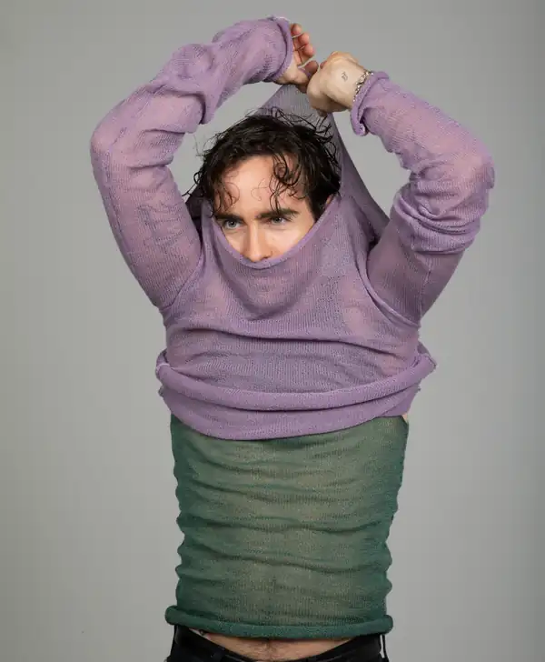 Pulling the lilac knit long-sleeve up over the head, sage-green knit beneath.