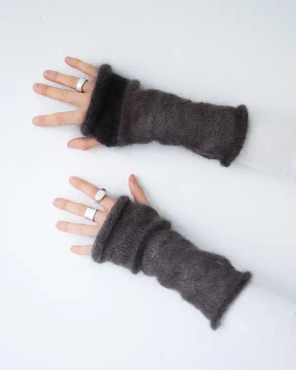 Flat lay on white: a pair of dark brown mohair fingerless arm warmers, with two hands wearing them.