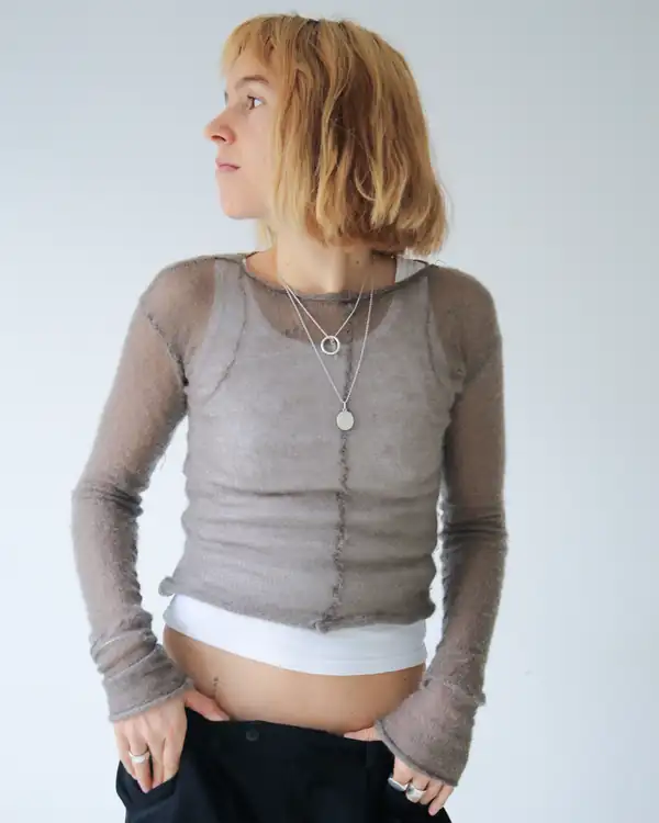 Taupe sheer knit long-sleeve with a centre seam over a white ribbed top and black trousers.