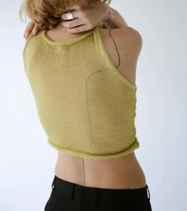 Chartreuse knit sleeveless top with a rolled hem and deep armhole, hand at the neck.