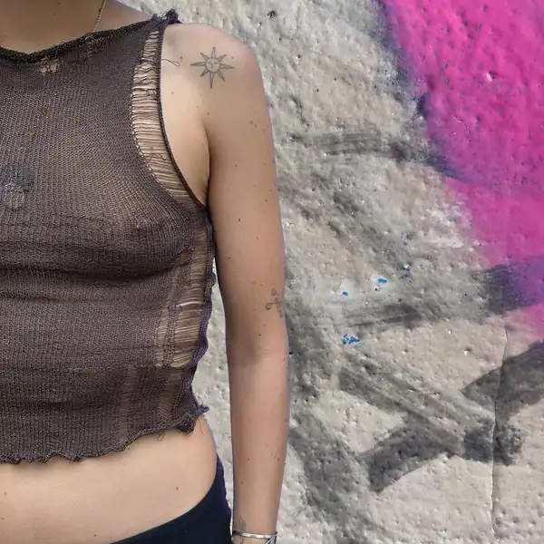 Side: brown sheer knit sleeveless top with a ladder detail up the side seam, graffitied wall behind.